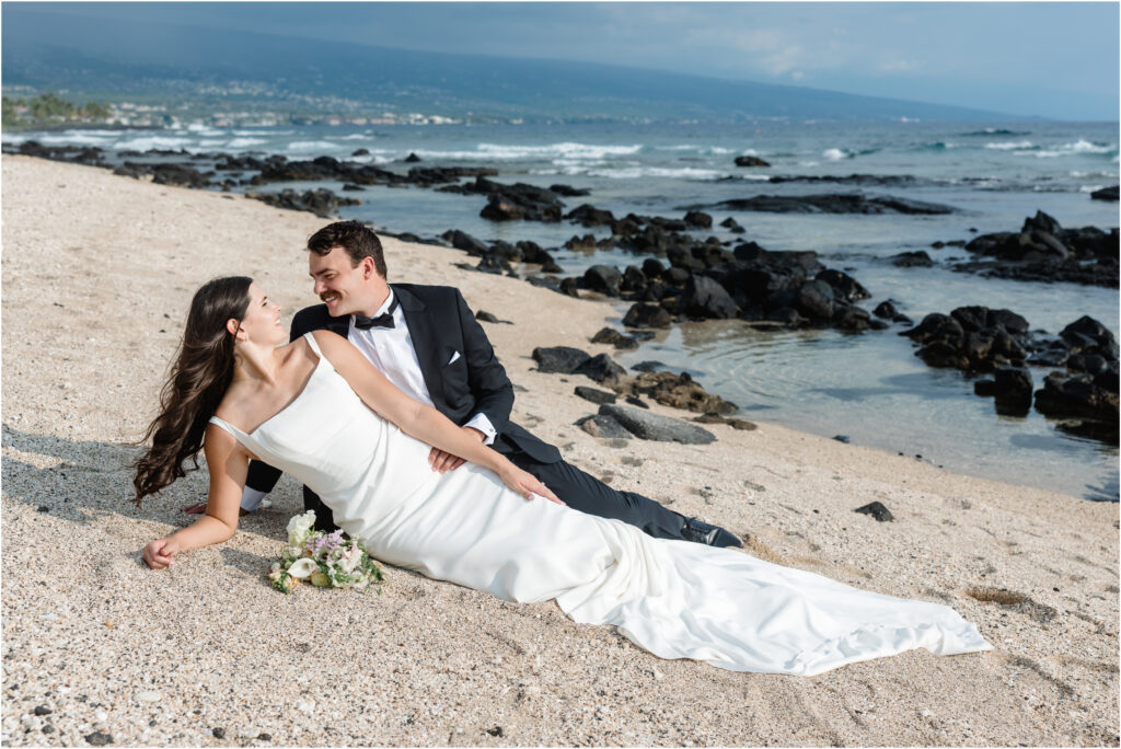 bride and groom reclining on sand in Hawaii