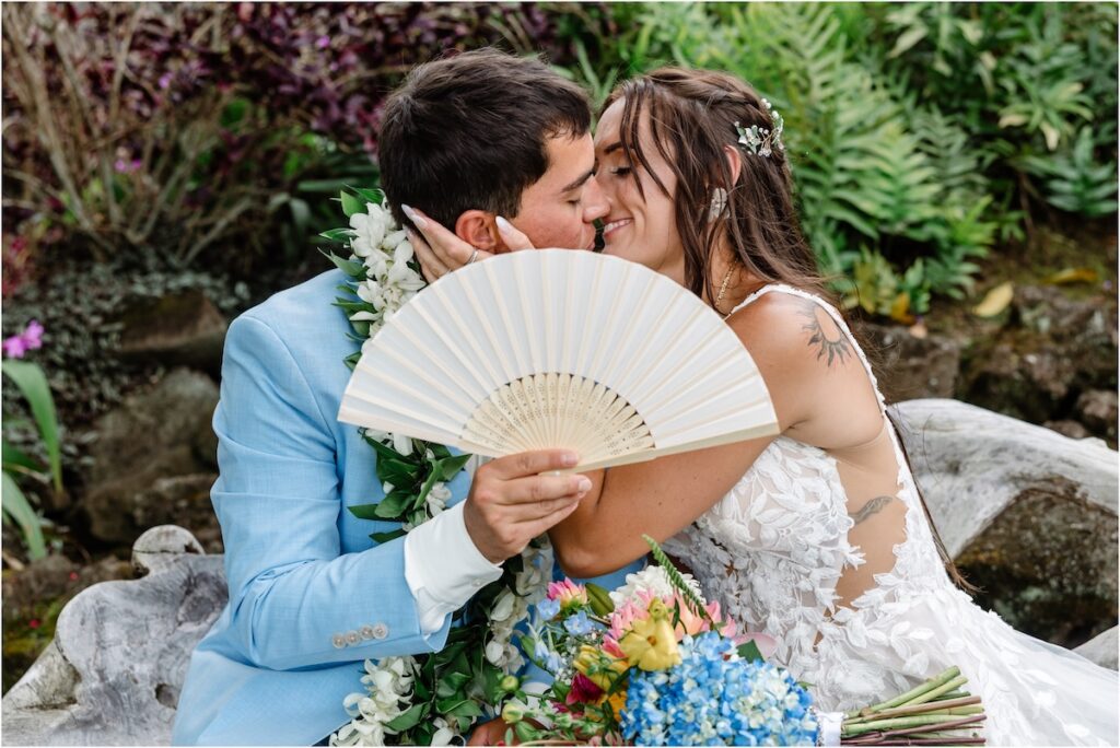 Bride and groom at Holualoa Inn Wedding art garden for couple's portraits, kissing behind a fan